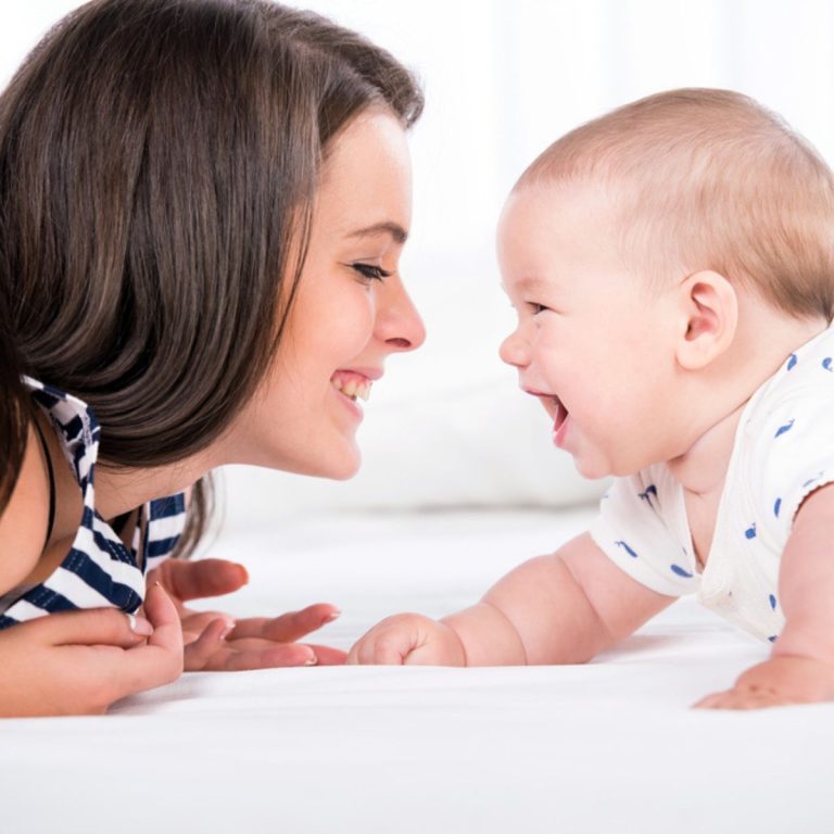 A baby laying on its stomach laughing at mom.
